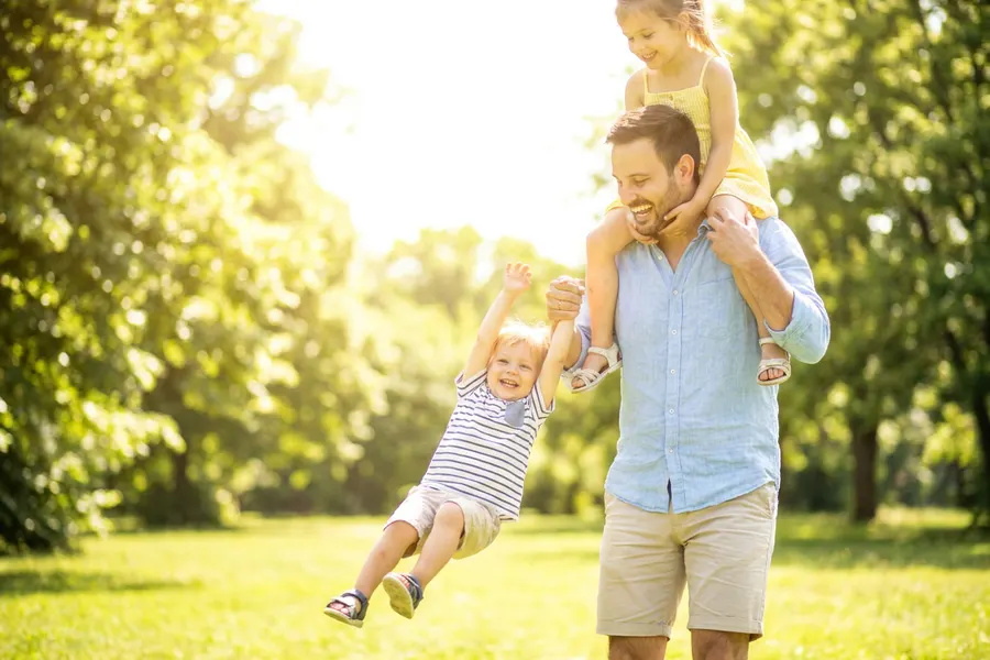 A man playing outdoors with his two young children in bright sunshine