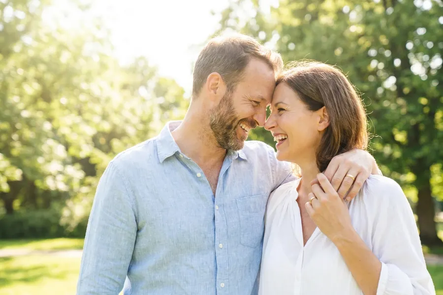 A married couple laughing together outdoors in bright sunlight