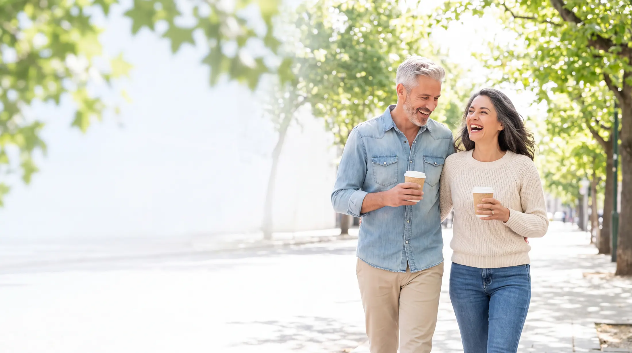 A couple in their fifties walking with coffee on a sunlit morning